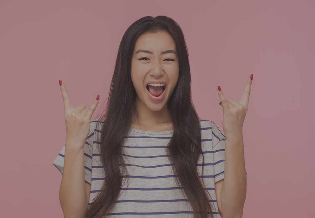 Portrait of delighted crazy girl with long hair in striped t-shirt showing rock and roll punk gesture