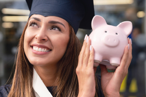 smiling college graduate holding a pink piggy bank