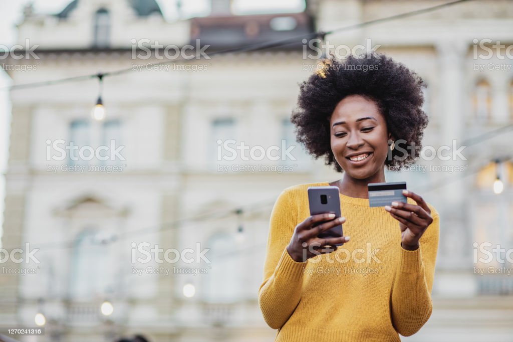 Photo of African American modern woman on the street holding smart phone and credit card