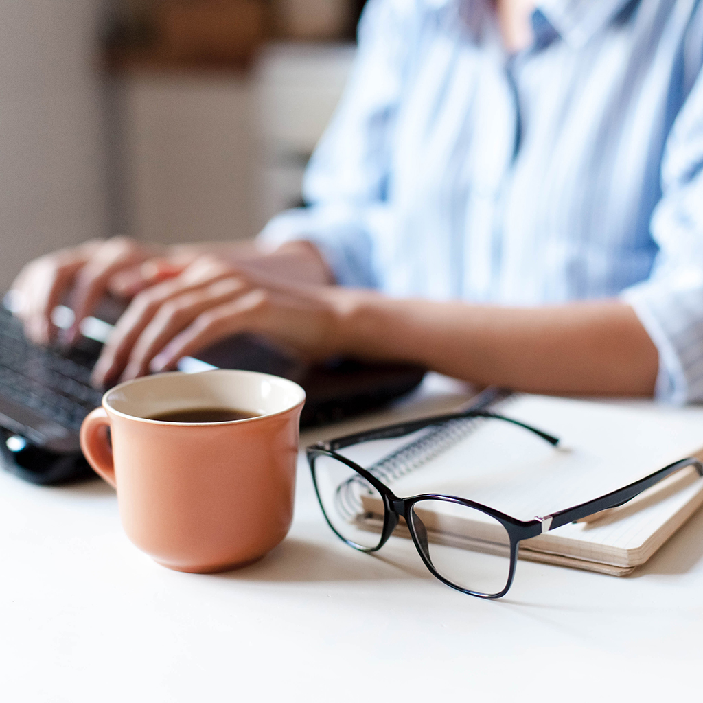 pair of glasses and cup of coffee on desk beside remote worker