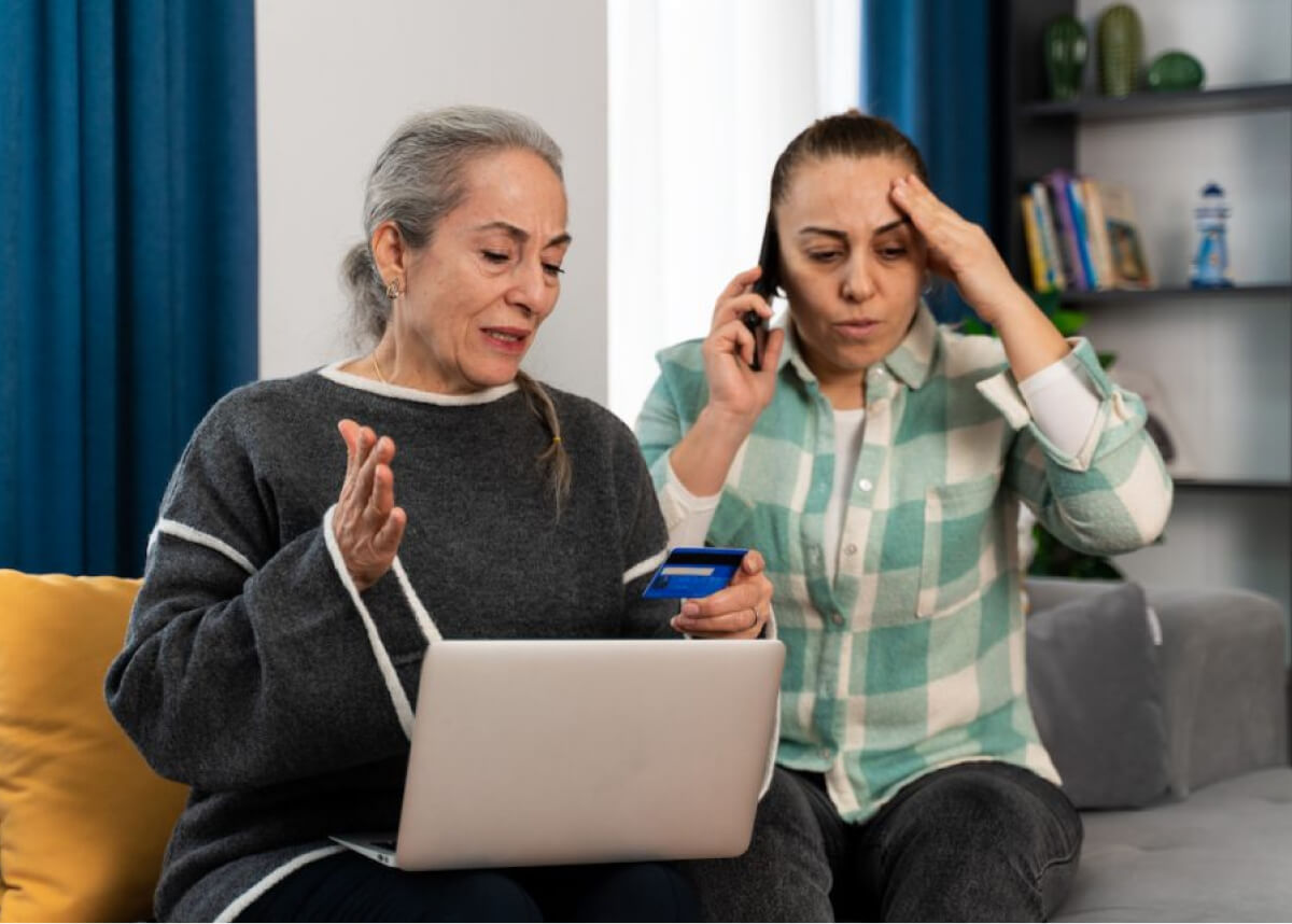 Two concerned women stand by a laptop.