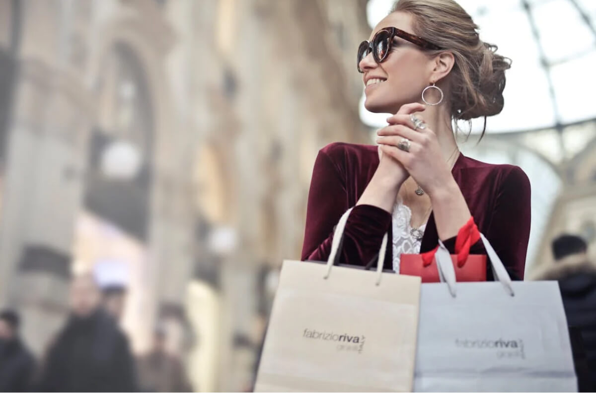 A woman wearing sunglasses holds several shopping bags.