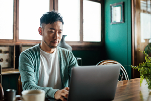 A man seated at a table, focused on his laptop.