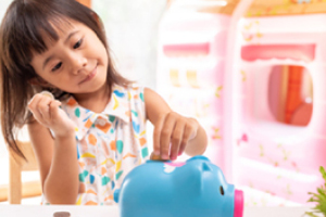 A young girl joyfully deposits coins into a piggy bank.