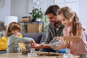 A man and two children joyfully playing with coins on a table.