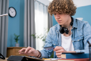 A young man wearing headphones is focused on his laptop.