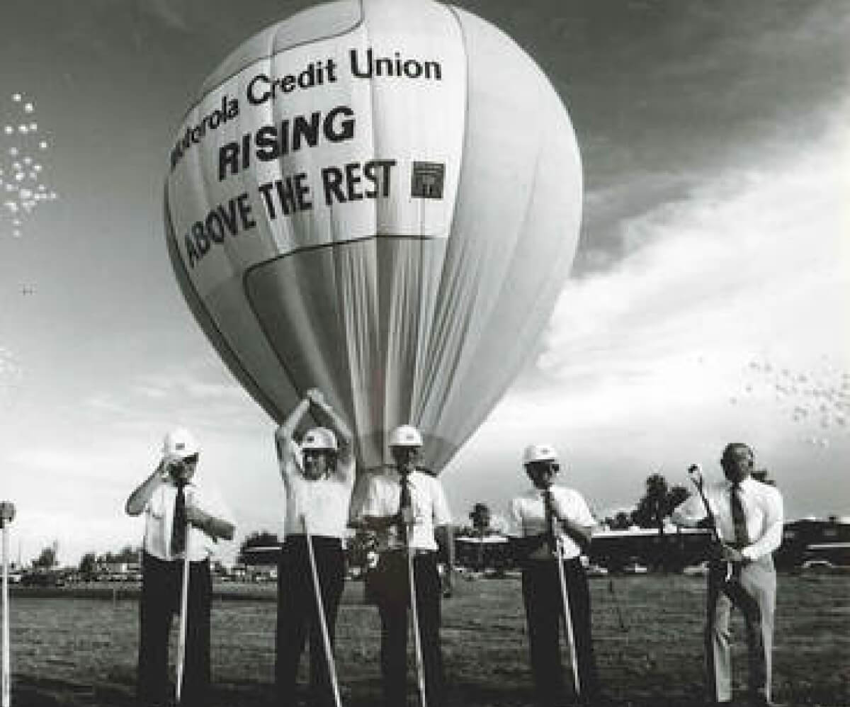 Five people wearing helmets stand in front of a large hot air balloon