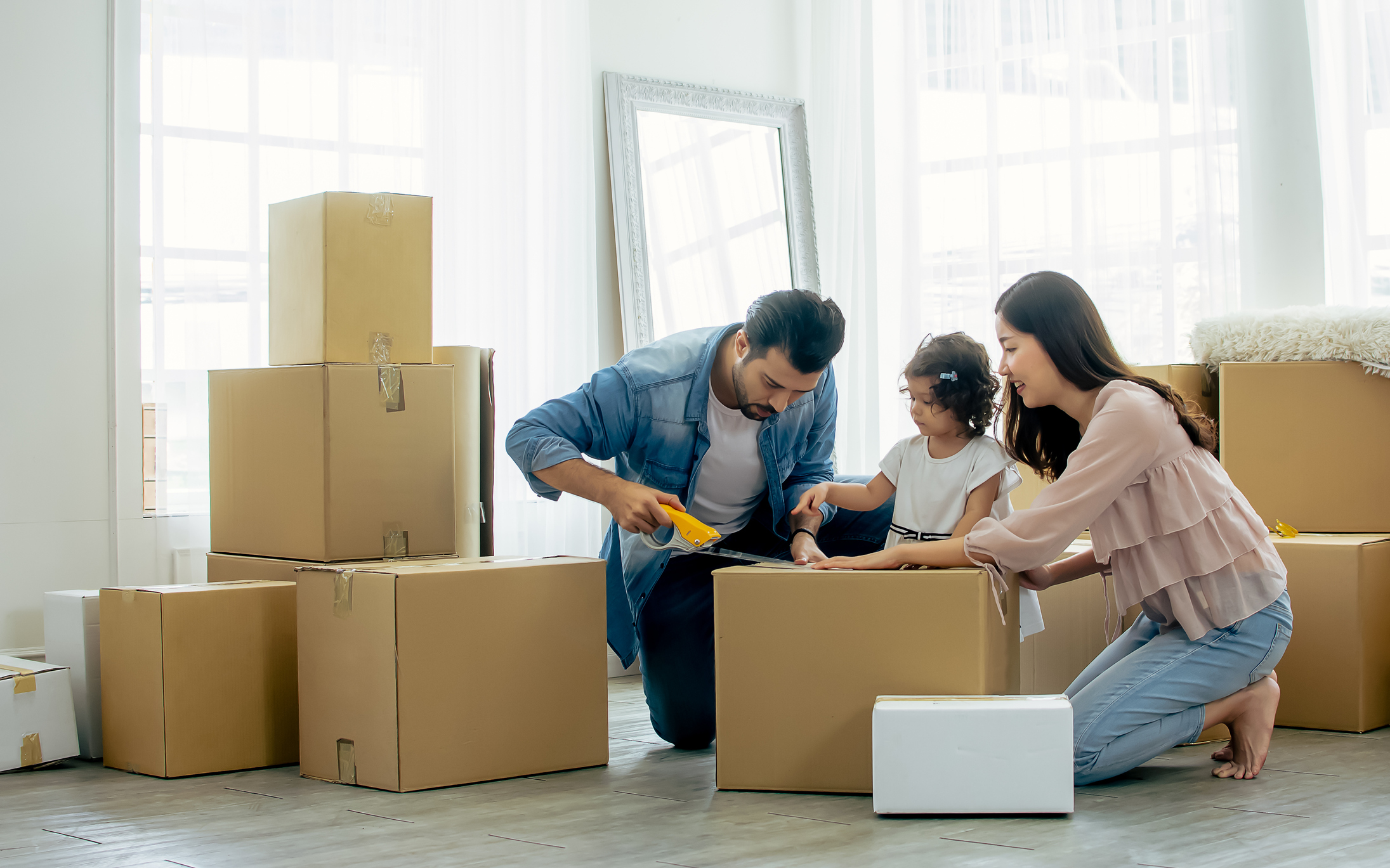 a father, mother, and daughter taping moving boxes inside their house