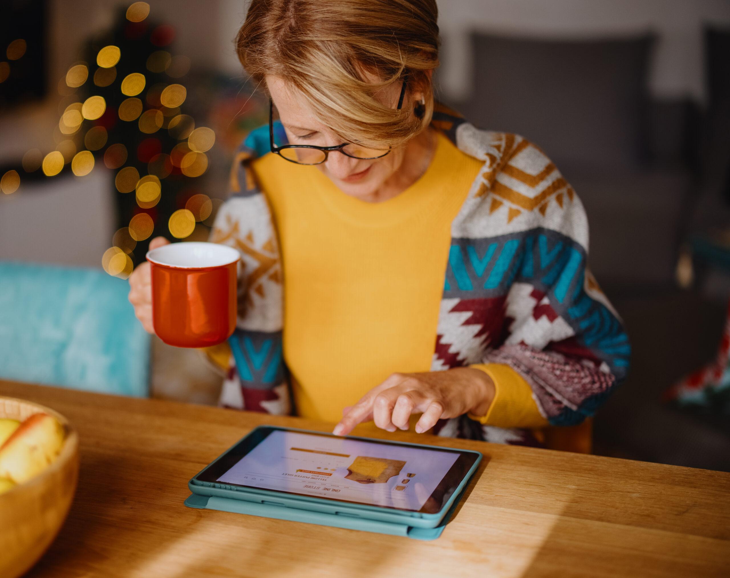 woman sitting at dining table with cup in her hand looking down at her tablet