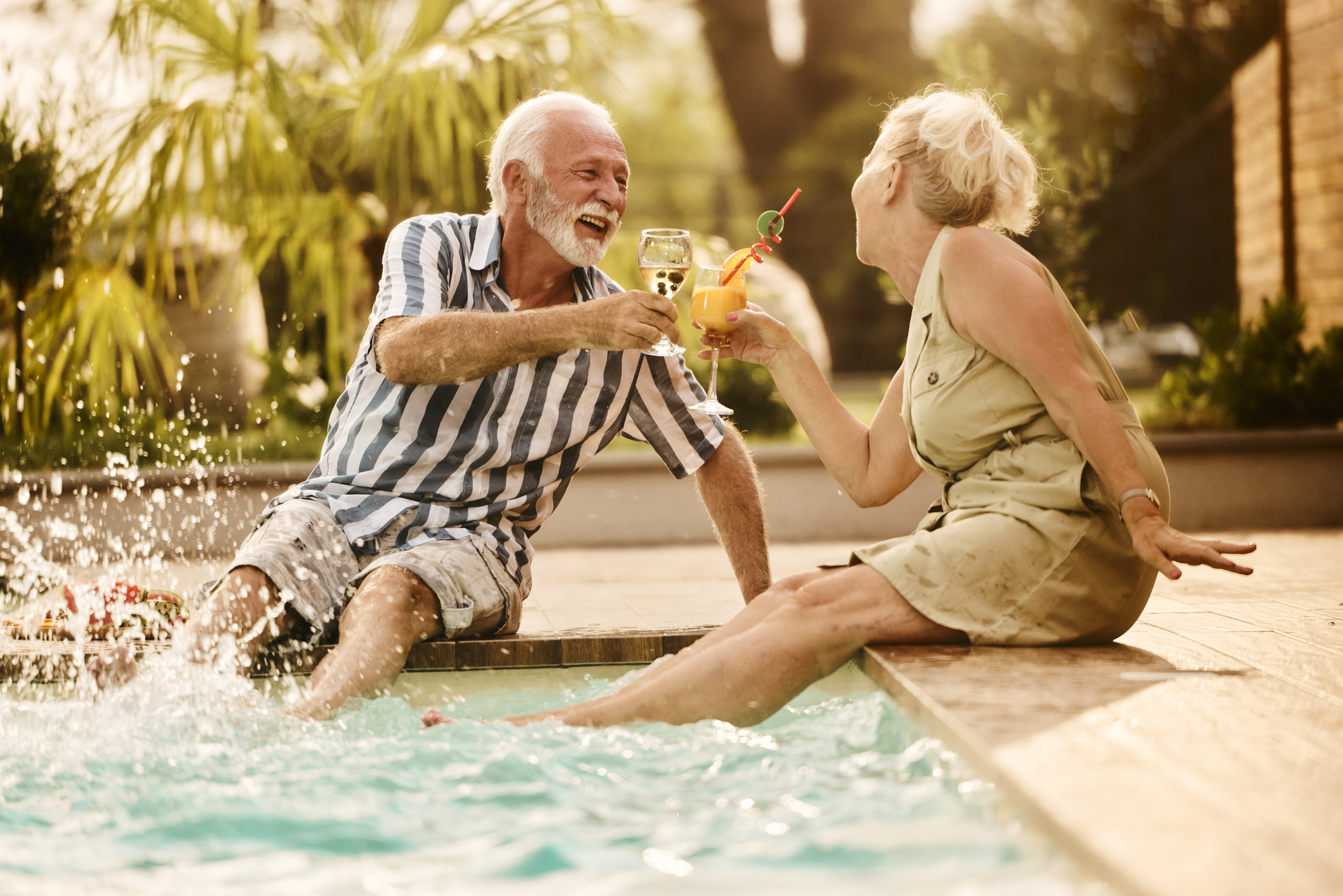 Playful senior couple toasting by the pool in summer day.